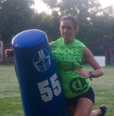 Katherine Foley in a lime green tank top running into a football tackling dummy.