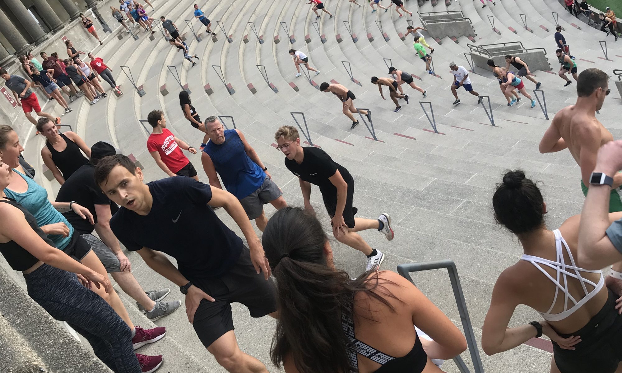 Many people climbing stairs in Harvard stadium, a colosseum-like structure. Everyone is working hard.