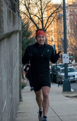 Young Joo running up a hill and holding up peace fingers and smiling.