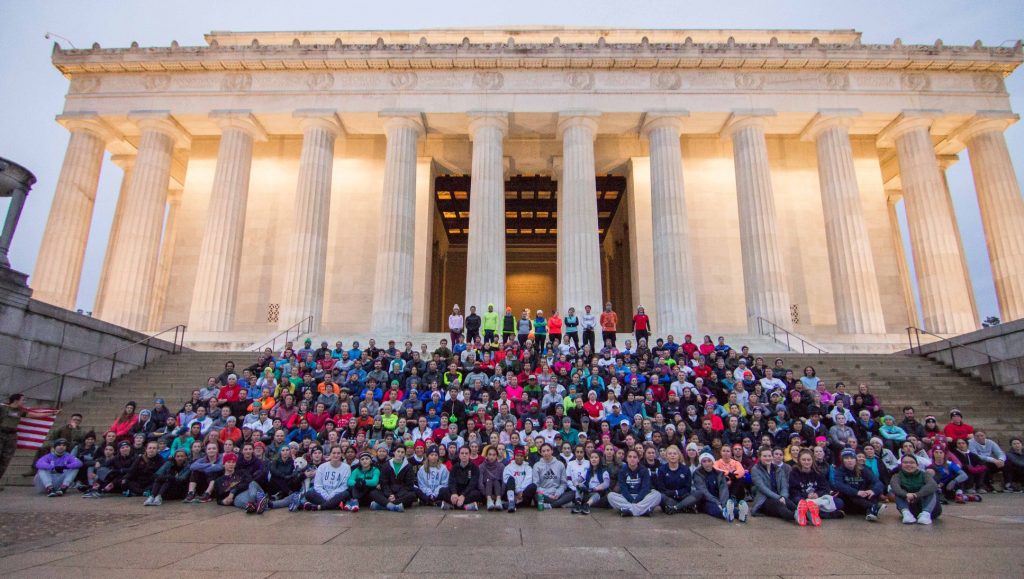 A very large group of people sit on the stairs of the Lincoln Memorial. 