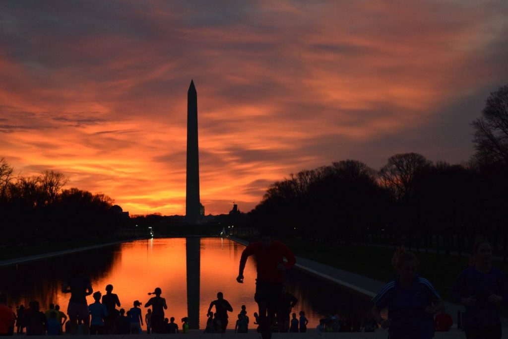 Silhouettes of people running up and down stairs with a glowing sky and the Washington Monument in the background. 
