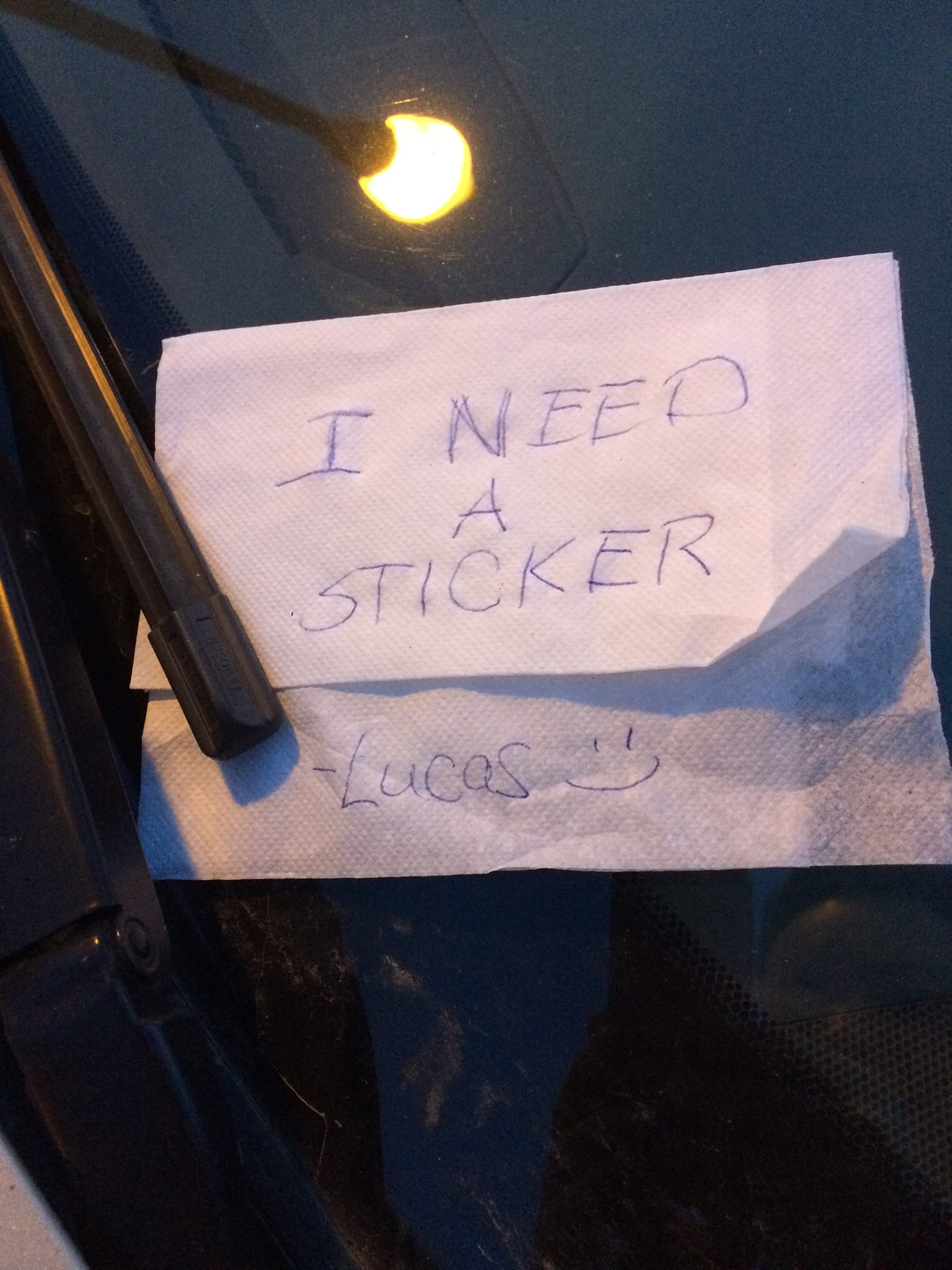 Lucas hand wrote a note on a napkin that he needed a sticker for the attendance challenge.  The note is on the windshield of Natalie's car.